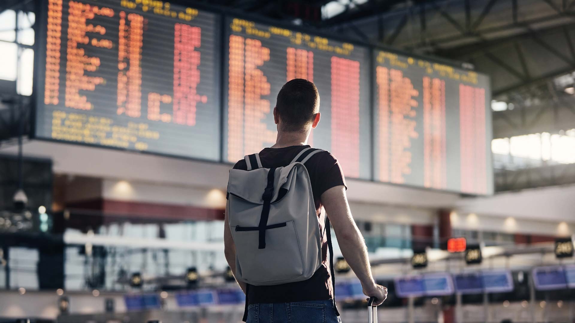 Traveler with a backpack watching the departure board above empty check-in desks in an airport terminal