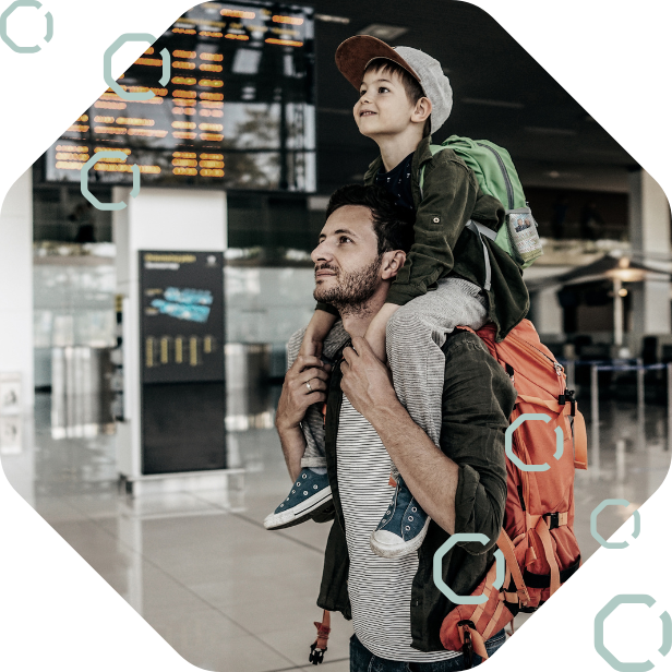 Father carrying his son on his shoulders as they read the departure board in an airport terminal