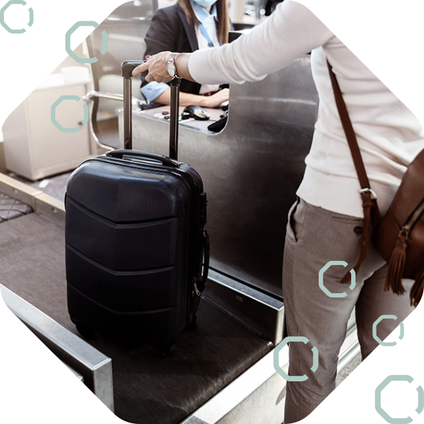 Passenger placing a suitcase on a check-in bag drop belt at an airport passenger processing counter.