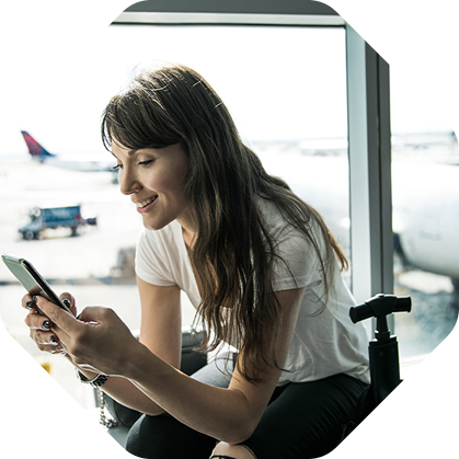 Female passenger sitting at airport gate using smartphone while waiting for boarding